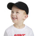 Nike kids' black cap worn by a smiling child with a white logo t-shirt in a studio setting.