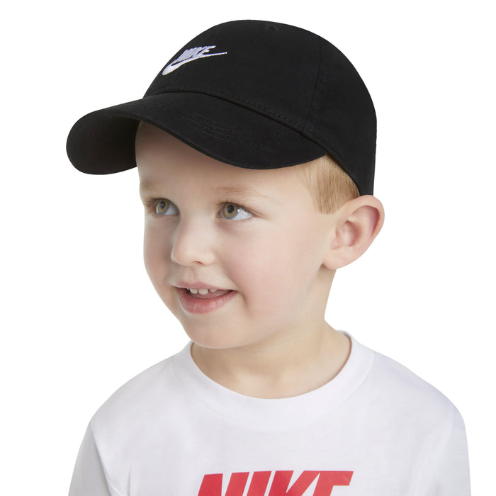Nike kids’ black cap worn by a smiling child with a white Nike t-shirt on a white background.