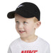 Nike kids’ black cap worn by a smiling child with a white Nike t-shirt on a white background.