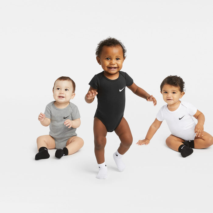 Nike baby bodysuits in black, grey, and white shown on three babies against a white background.