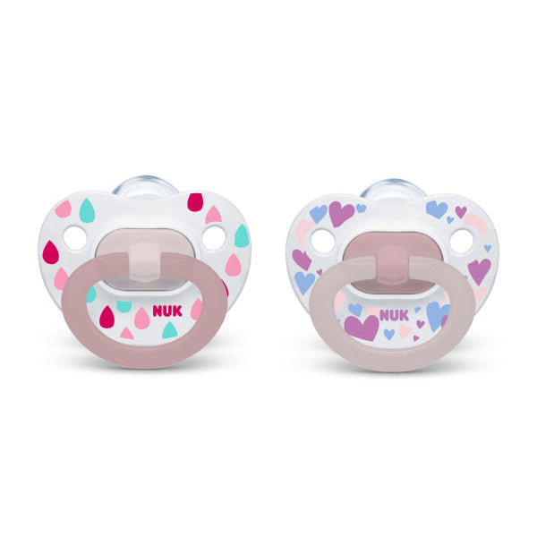 NUK pacifiers with pink and pastel heart and raindrop patterns shown side by side on white background.