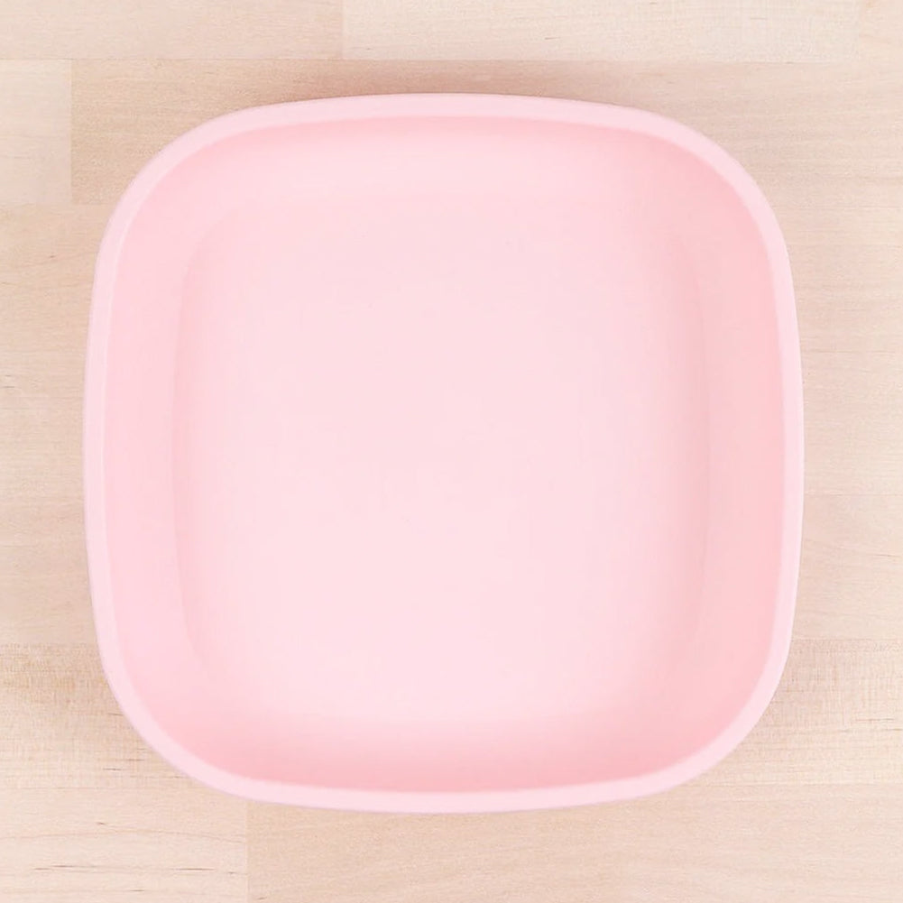 Square pink kids flat plate on light wood surface, children’s dinnerware