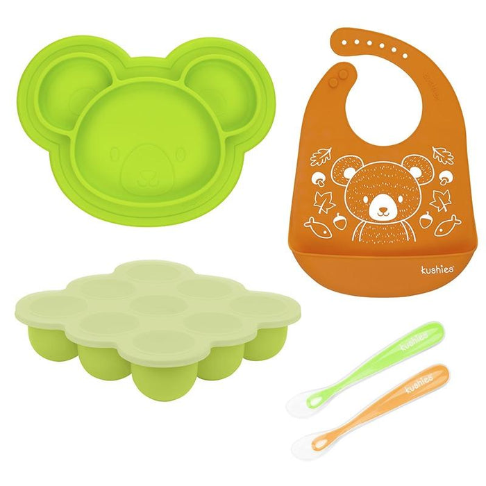 Kushies baby feeding set with green bear-shaped plate, orange bib, freezer tray, and two spoons on white background.