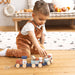 Stacking train toy in use by a young child sitting on a wooden floor in a cozy playroom.