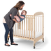 Woman placing smiling baby in natural wood crib with clear side panel and wheels