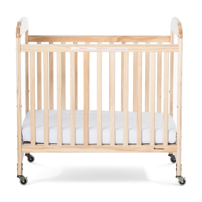 Natural wood daycare crib with clear end panels, slatted sides, and locking caster wheels