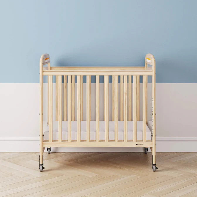 Natural wood crib with clear side panels and wheels in a modern nursery with blue and white walls