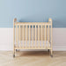 Natural wood crib with clear side panels and wheels in a modern nursery with blue and white walls