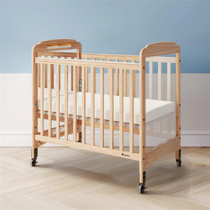 Natural wood crib with wheels and white mattress in bright nursery room