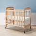 Natural wood crib with wheels and white mattress in bright nursery room