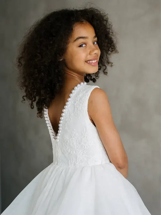 Sunny JK07 Pearl Back Horsehair Communion Dress shown on a smiling girl facing away, highlighting pearl details.