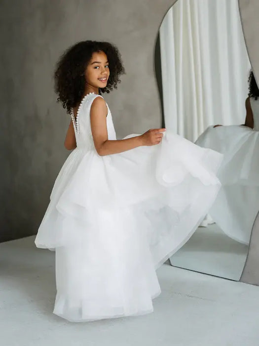 Sunny JK07 Pearl Back Horsehair Communion Dress shown on a smiling girl standing beside a mirror.