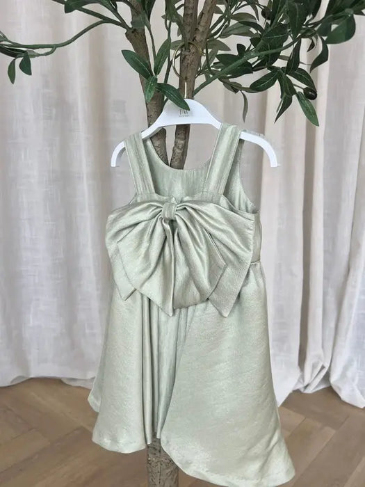 Teter Warm Clarice sage green party dress with large bow displayed on hanger in front of tree.