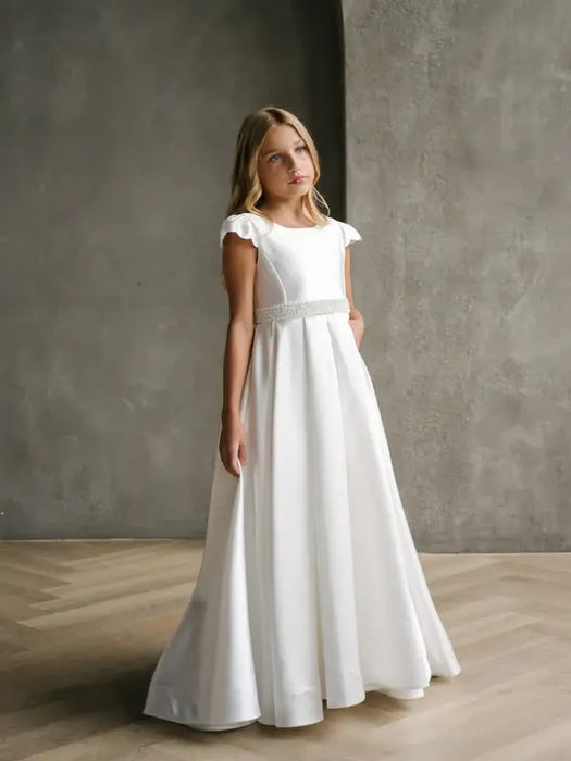 Teter Warm Charlotte satin communion dress shown on a girl standing in a minimalist indoor setting.