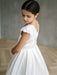 Teter Warm Charlotte satin communion dress on a young girl standing indoors, facing away.