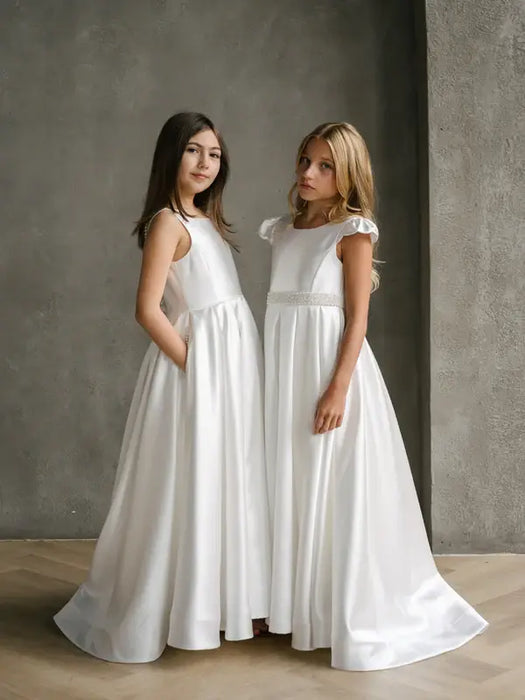 Charlotte satin communion dress shown on two girls standing indoors against a plain gray wall.