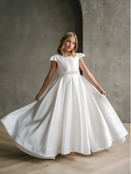 Teter Warm Charlotte satin communion dress displayed on a girl standing indoors against a gray wall.