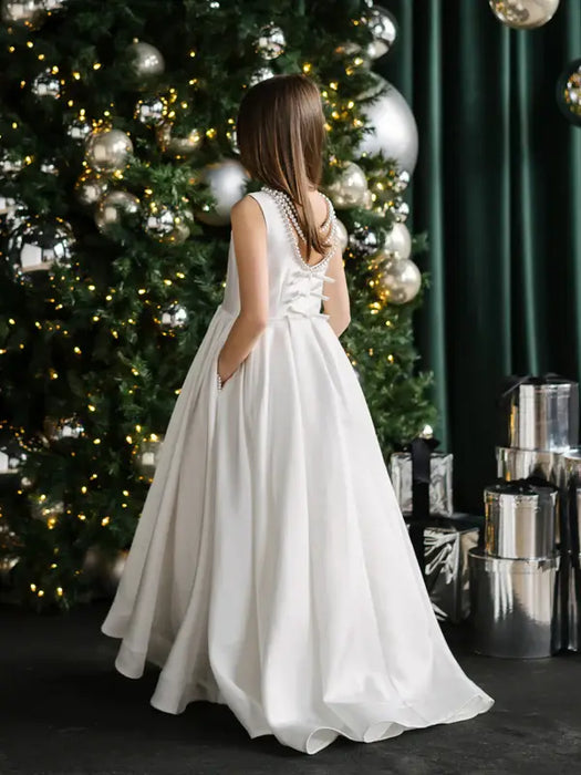 Teter warm off-white communion dress shown on a girl standing by a decorated Christmas tree.