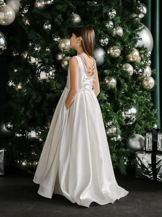 Teter warm off-white communion dress shown on a girl standing in front of a decorated Christmas tree.