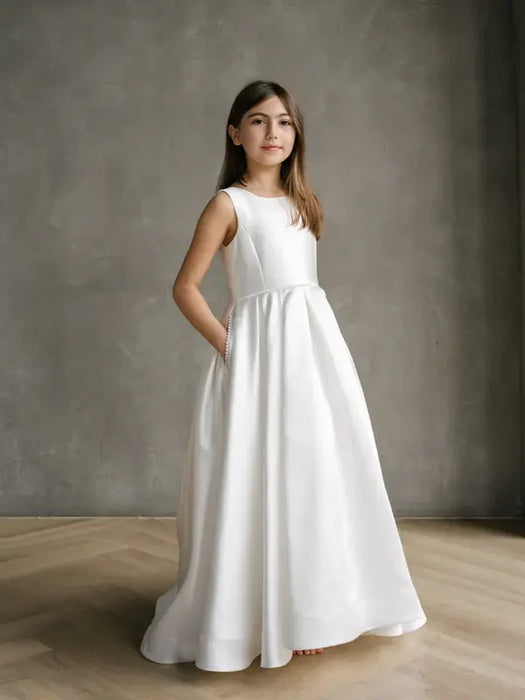Teter warm off white communion dress worn by a girl standing indoors against a grey wall.