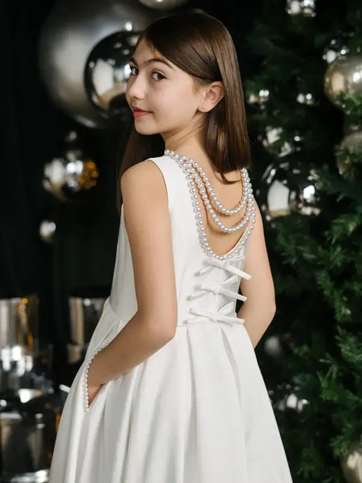 Teter warm off white communion dress with pearl back detail, shown on a girl beside a decorated tree.