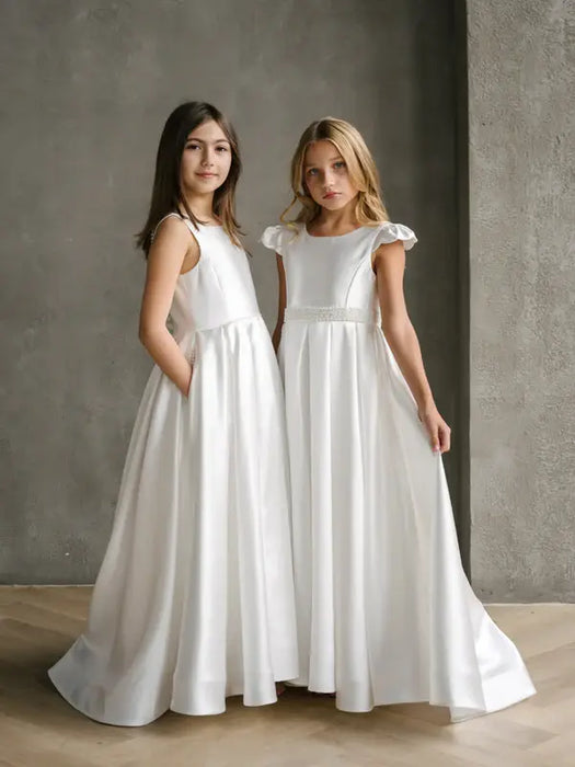 Teter warm off white communion dress shown worn by two girls standing indoors against a gray wall.