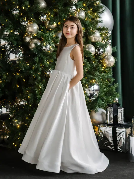 Teter warm off white communion dress worn by a girl standing beside a decorated Christmas tree.
