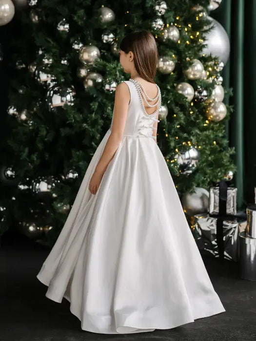 Teter warm off white communion dress with pearl back shown on a girl standing near a decorated Christmas tree.