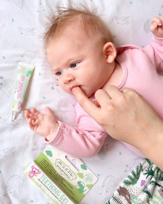 Jack N' Jill Teething Gel applied to a baby's gums while lying on a patterned crib sheet.