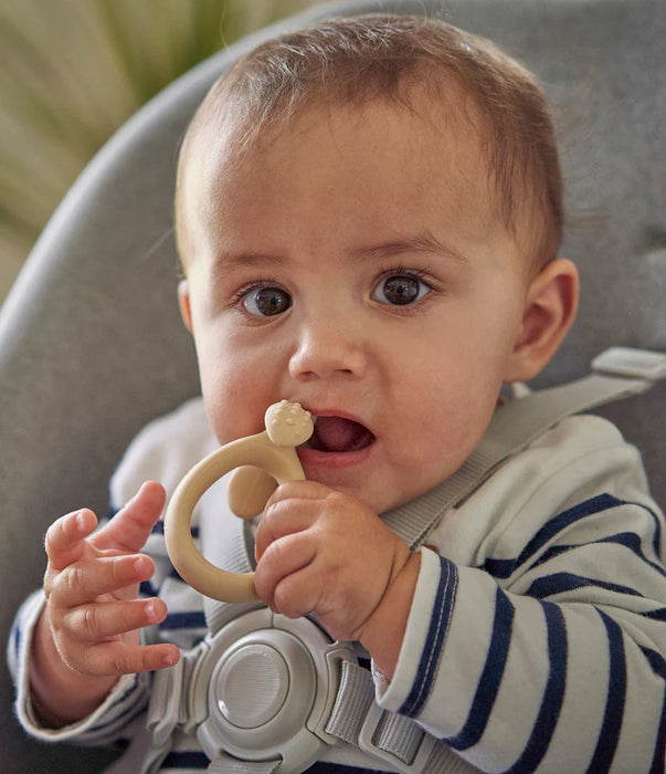 Baby in striped onesie holding beige teething ring, sitting in high chair