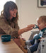 Smiling woman feeding baby in high chair with silicone bib and bowl, toddler feeding time
