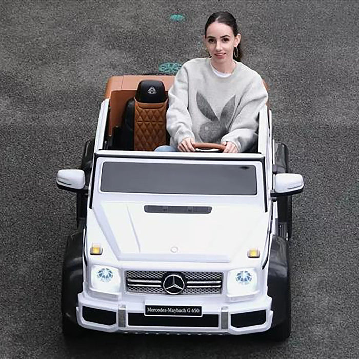 Mercedes-Maybach G 650 kids ride-on car in white driven outdoors by a young woman on pavement.