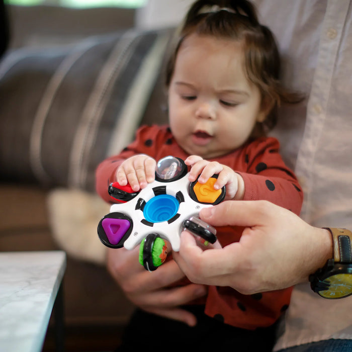 b.box baby sensory toy being held by an adult as a baby explores it in a living room setting.