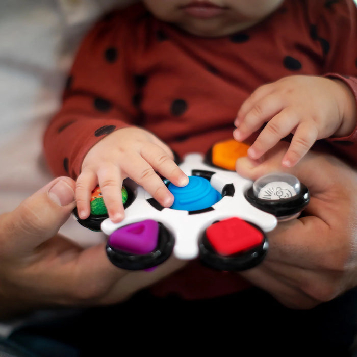 b.box baby sensory toy clutch held by a baby, colorful textured buttons, adult hands supporting.