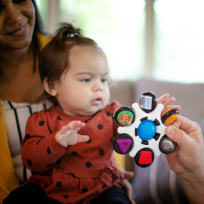 b.box baby sensory toy clutch held out to an infant sitting with an adult on a couch
