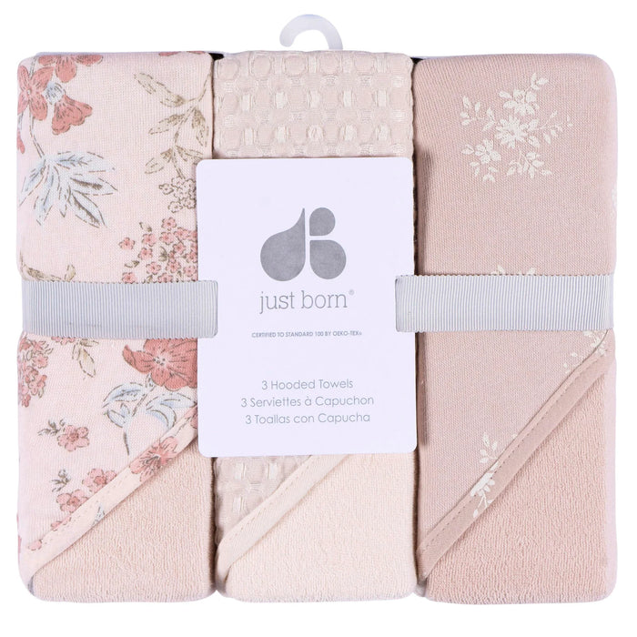 Just Born hooded baby towels three-pack with floral patterns and soft pink hues, neatly packaged.