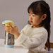 b.box insulated water bottle with Looney Tunes design held by a young child at a table.