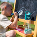 b.box kids tritan drink bottle with teal lid on an art easel beside a child drawing outdoors
