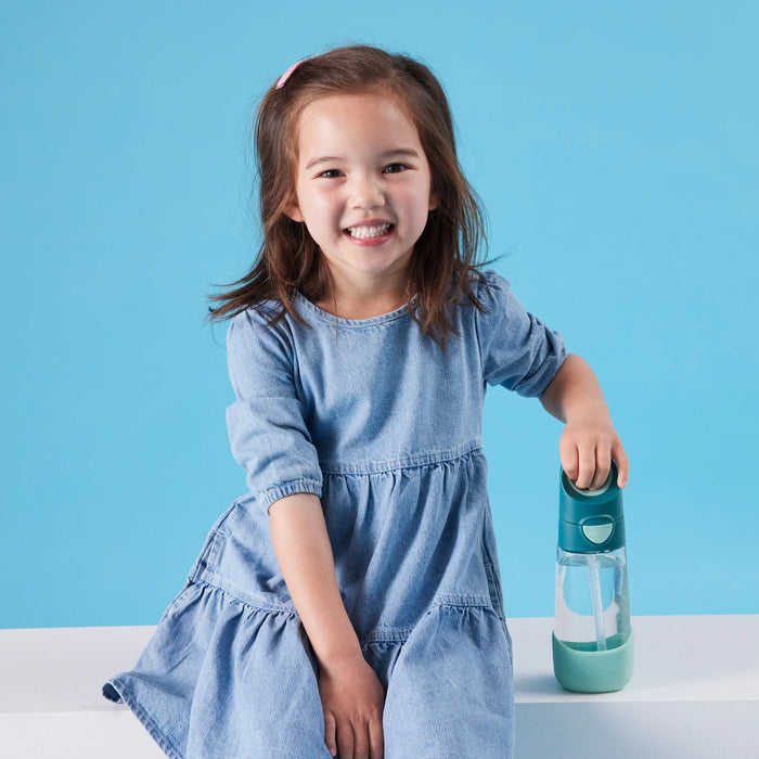 b.box kids tritan drink bottle shown upright on a white surface beside a smiling child in a blue dress.