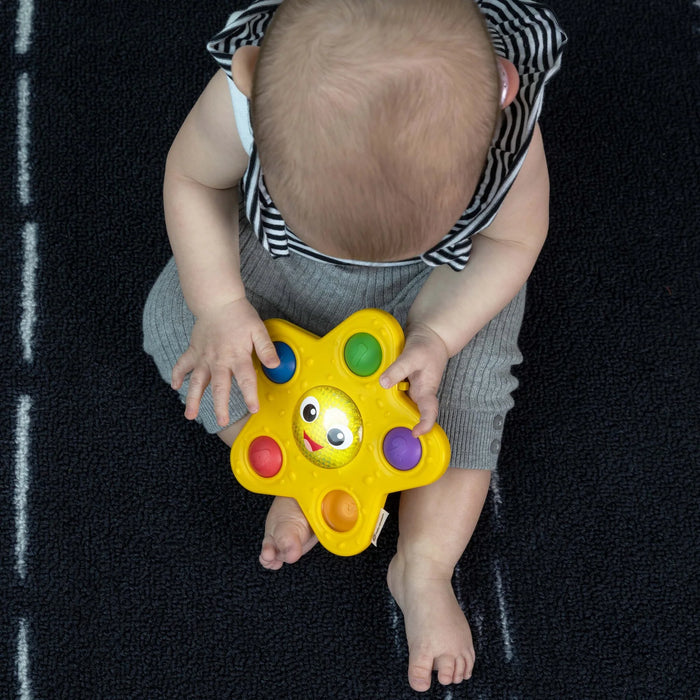 b.box Pop & Glow Starfish Sensory Toy held by a baby sitting on a dark textured carpet.