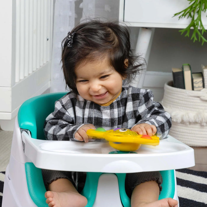 b.box pop & glow starfish sensory toy held by smiling baby at a high chair tray in a nursery.
