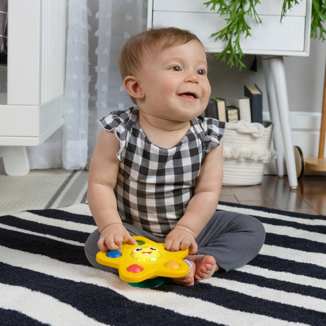 b.box Pop & Glow Starfish Sensory Toy in use by a smiling baby sitting on a striped rug indoors.