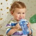 NUK blue sippy cup being used by a toddler in a colorful striped shirt indoors.