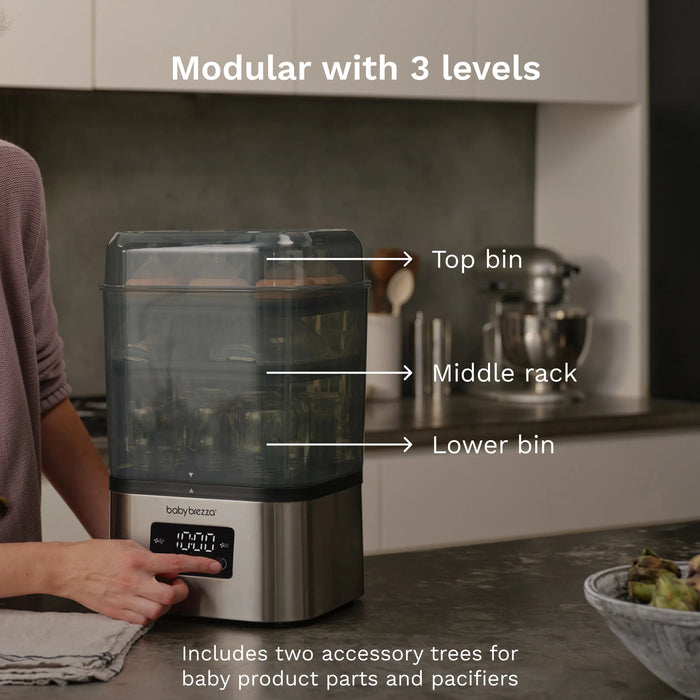Baby Brezza Super Fast Sterilizer and Dryer on a kitchen countertop with a person using the control panel.