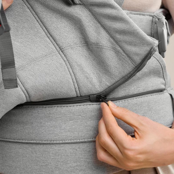 Close-up of a hand zipping a light grey baby carrier with adjustable padded straps
