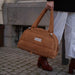 Baby On Board doudoune diaper bag in tan suede carried by a person outdoors on a sidewalk.