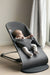 BabyBjorn charcoal baby bouncer with a baby seated indoors near a window and curtain.