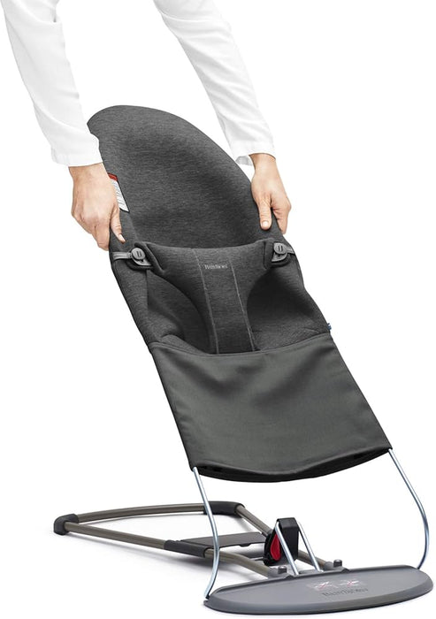 BabyBjorn charcoal baby bouncer being adjusted by hands on a white background.