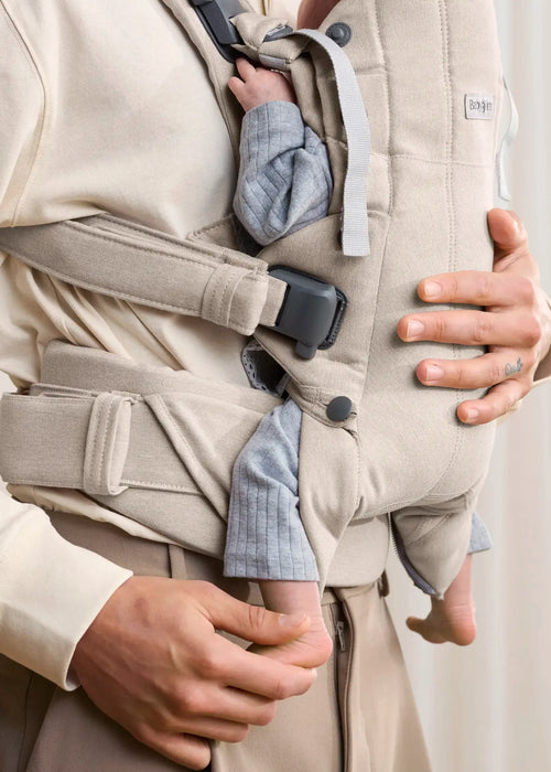 BabyBjorn Harmony baby carrier in beige with baby worn on adult's chest, close-up view.
