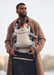 BabyBjorn Harmony baby carrier in beige worn by a man carrying an infant outdoors.